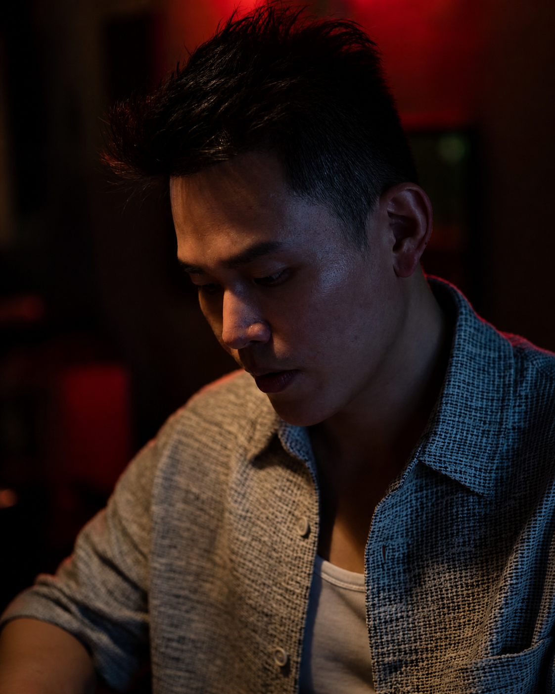 Cinematic close-up. Alvin in a textured tweed shirt, head turned downward in warm red light