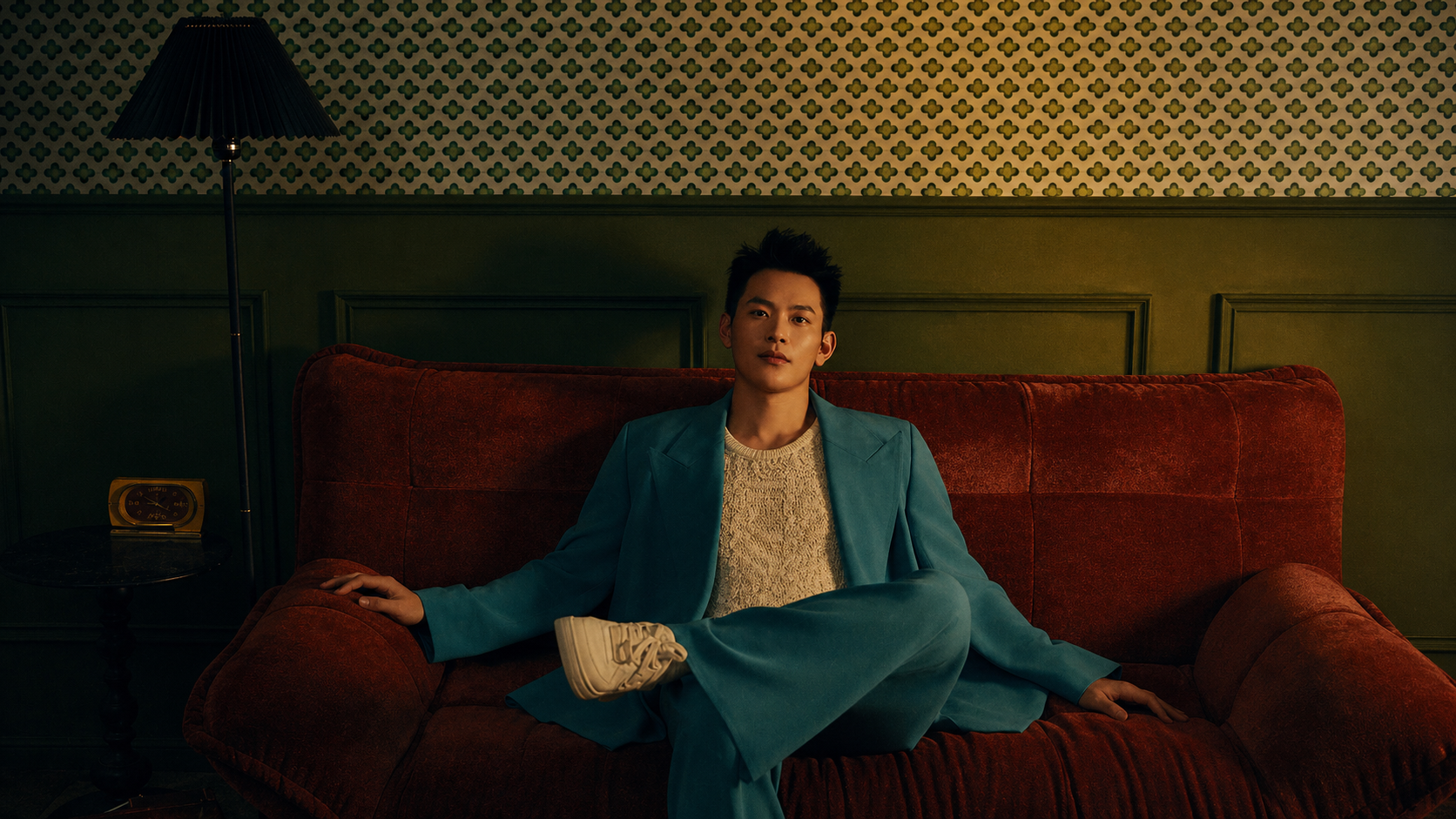 Alvin Julian Tan, editorial portrait. Seated on a velvet sofa in a tailored teal suit, looking directly at camera