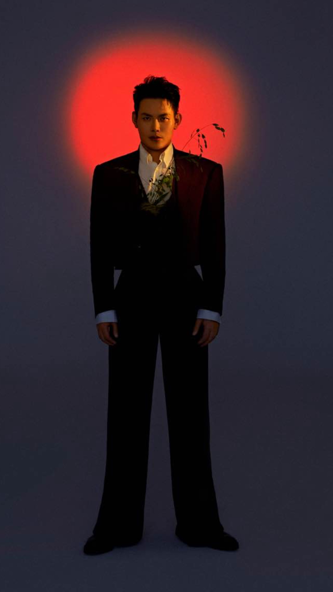 Alvin in a dark suit standing under a red sun-disc halo against a grey backdrop