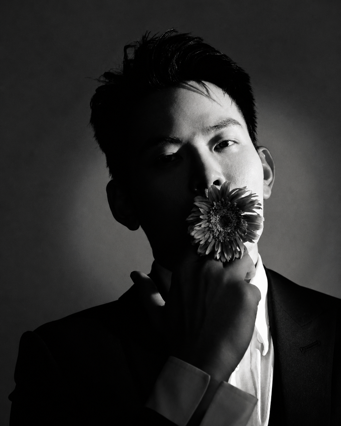 Black-and-white chiaroscuro portrait. Alvin holding a gerbera flower at his cheek