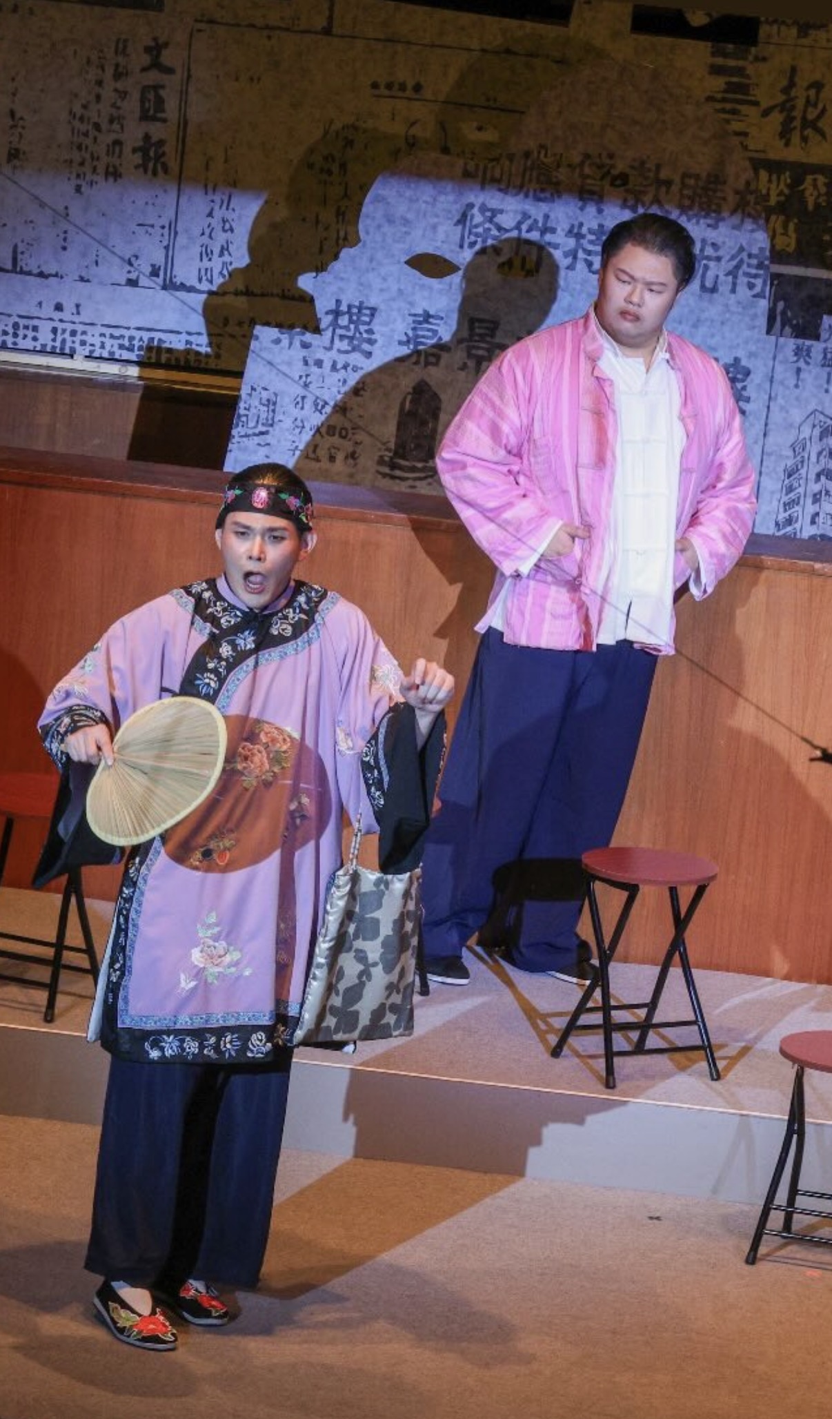 Alvin as Kecal in lavender embroidered robe and matchmaker's headdress, fan in hand, with another performer behind